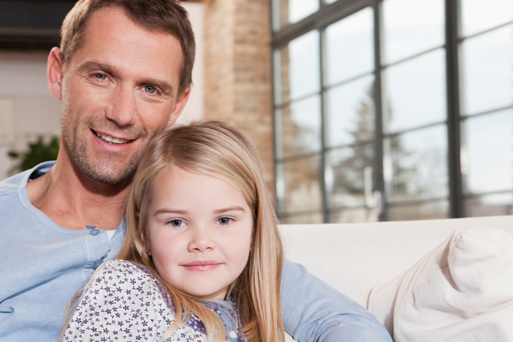 Father and daughter sitting on sofa embracing smiling close-up